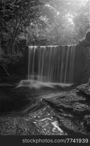 Black and white Stunning beautiful Autumn landscape image of Nant Mill waterfall in Wales with glowing sunlight through the woodland