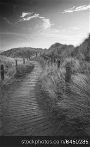 Black and white sunrise landscape image of sand dunes system over beach with wooden boardwalk