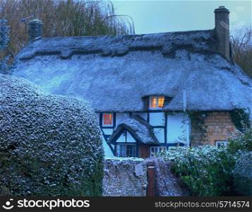 Black and white, timber-framed thatched cottage in winter, Mickleton near Chipping Campden, Gloucestershire, England.