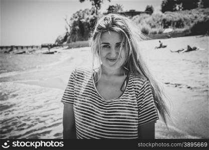 Black and white toned portrait of cute woman with long hair in striped sailor shirt posing on beach