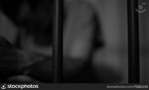 Black and white view of an inmate in prison hold tightly onto bars