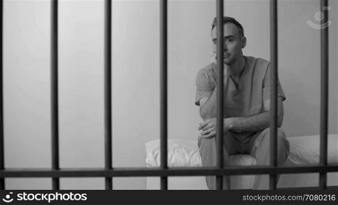 Black and white view of gloomy inmate in prison seated on his bed