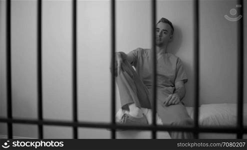 Black and white view of Lonely inmate sitting on bed in prison
