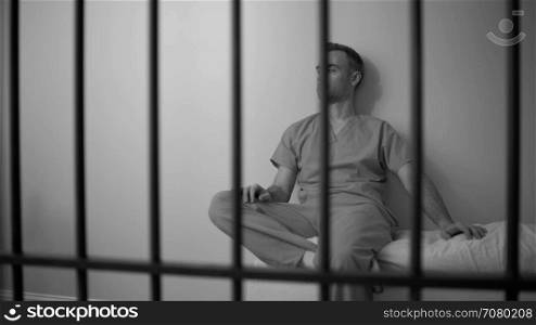Black and white view of remorseful inmate sitting on bed in prison