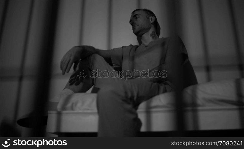 Black and white view of scene of a depressed and tattooed inmate in prison
