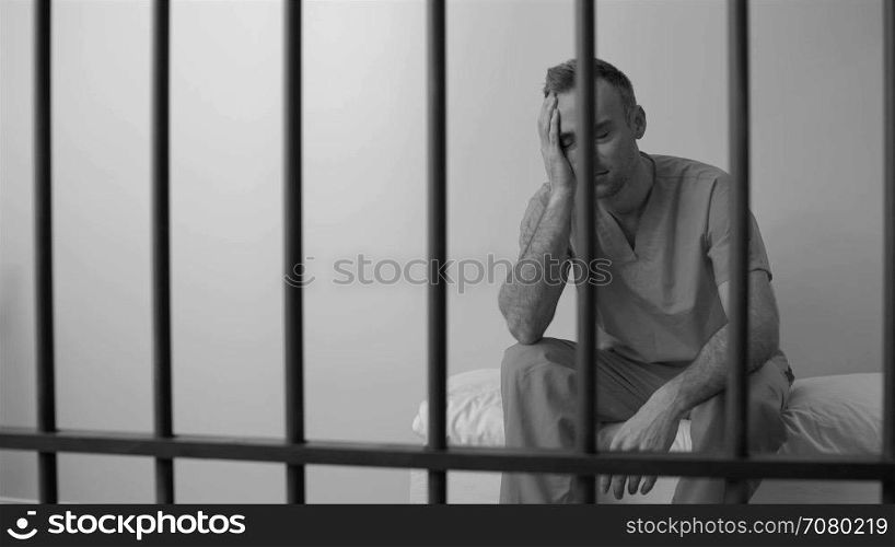 Black and white view of scene of a moody inmate in prison on bed