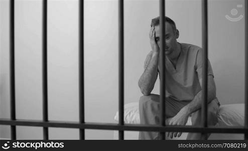 Black and white view of scene of a moody inmate in prison on bed