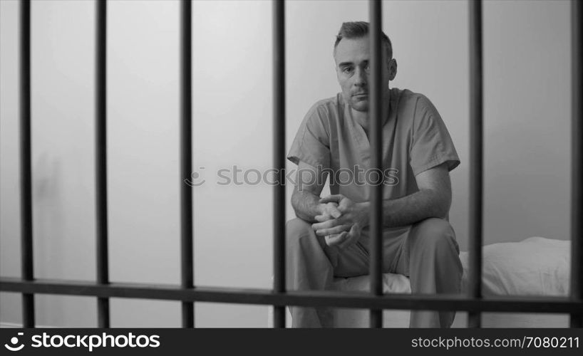 Black and white view of somber inmate sitting on bed in prison