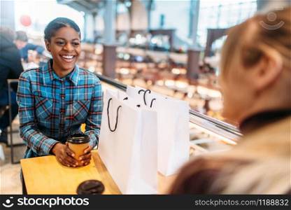 Black and white women in food-court after shopping. Shopaholics in clothing store, consumerism lifestyle, fashion, female shoppers with bags