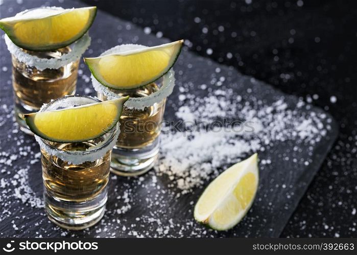 Black background with tequila glasses scattered with salt and lime. Alcoholic cocktail. Mexican traditional drink. Black background with tequila glasses scattered with salt and li