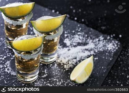 Black background with tequila glasses scattered with salt and lime. Alcoholic cocktail. Mexican traditional drink. Black background with tequila glasses scattered with salt and li