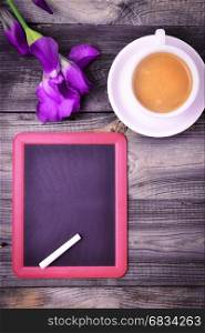 Black board with a piece of chalk and a cup of coffee on a gray wooden surface, top view