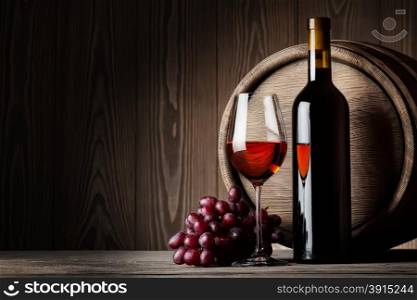 Black bottle and glass of red wine with grapes and barrel on wooden background. Black bottle and glass of red wine with grapes and barrel
