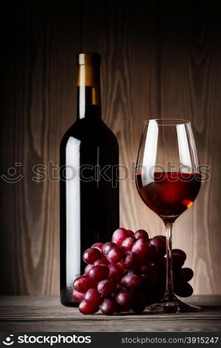 Black bottle and glass of red wine with grapes on wooden background. Black bottle and glass of red wine with grapes