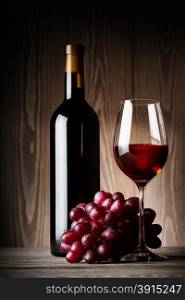 Black bottle and glass of red wine with grapes on wooden background. Black bottle and glass of red wine with grapes