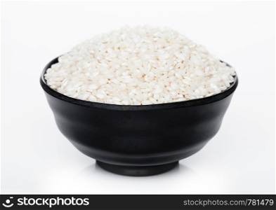 Black bowl of raw organic arborio risotto rice on white background.