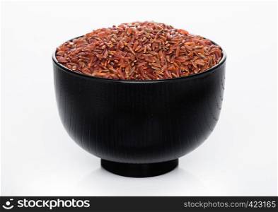 Black bowl of raw organic red rice on white background.