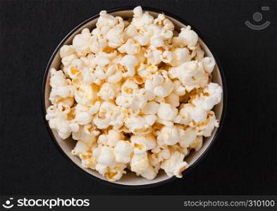 Black bowl with fresh salted popcorn on wooden background