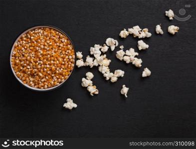 Black bowl with raw sweet corn and popcorn on black wooden background