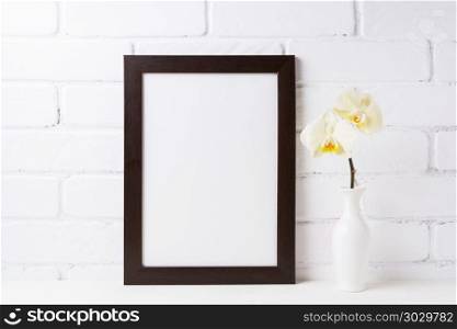 Black brown frame mockup with soft yellow orchid in vase. Empty frame mock up for presentation design. Template framing for modern art.. Black brown frame mockup with soft yellow orchid in vase