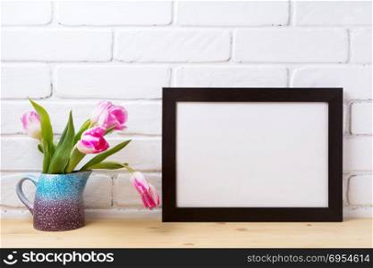 Black brown landscape frame mockup with pink tulip in the purple blue pitcher vase. Empty frame mock up for presentation design. Template framing for modern art.