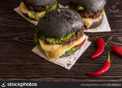 Black burger with beef meat cheese lettuce onion, tomato and sauce served on black wooden table