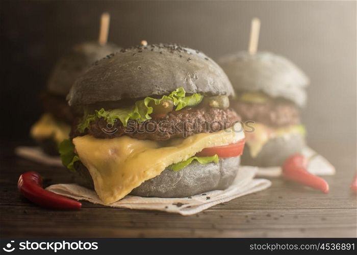 Black burger with beef meat cheese lettuce onion, tomato and sauce served on black wooden table