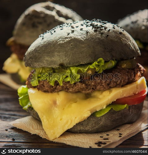 Black burger with beef meat cheese lettuce onion, tomato and sauce served on black wooden table