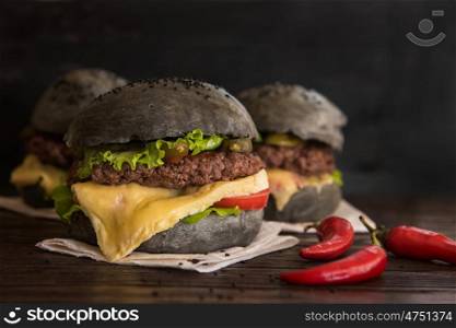 Black burger with beef meat cheese lettuce onion, tomato and sauce served on black wooden table
