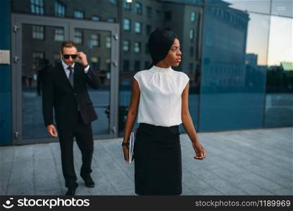Black business woman bodyguard in suit and sunglasses on background. Security guard is a risky profession, protection of VIPs, guarding occupation, private safety. Business woman, bodyguard in suit on background
