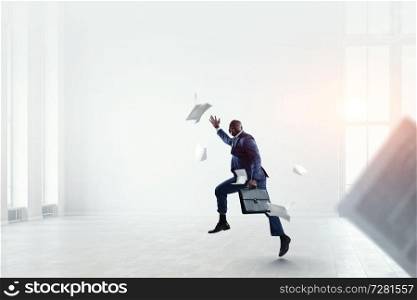 Black businessman in blue suit with briefcase running among flying documents in office. Black businessman with briefcase running among flying papers indoor