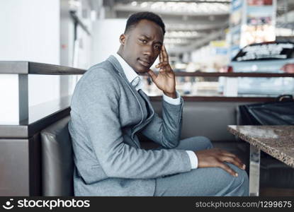 Black businessman in suit sitting in car showroom. Successful business person on motor show, man in formal wear, waiting area