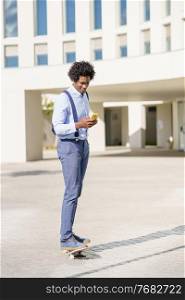 Black businessman on a skateboard looking at his smartphone near an office building.. Black businessman on a skateboard looking at his smartphone outdoors.