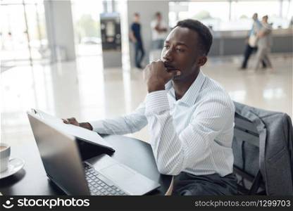 Black businessman sitting at laptop in car dealership. Successful business person on motor show, black man in formal wear, automobile showroom. Black businessman at laptop in car dealership