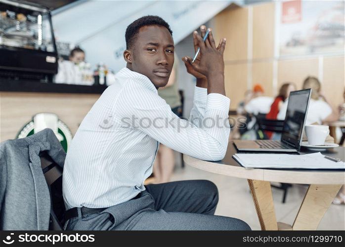 Black businessman sitting at laptop in car dealership. Successful business person on motor show, black man in formal wear, automobile showroom. Black businessman at laptop in car dealership