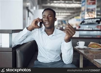 Black businessman talking by phone, car showroom. Successful business person on motor show, black man in formal wear. Black businessman talking by phone, car showroom