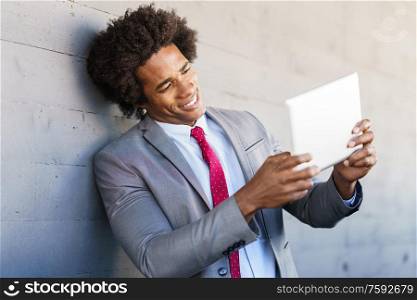 Black Businessman using a digital tablet in urban background. Man with afro hair.. Black Businessman using a digital tablet in urban background