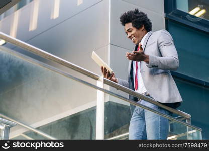 Black Businessman using a digital tablet sitting near an office building. Man with afro hair.. Black Businessman using a digital tablet sitting near an office building.