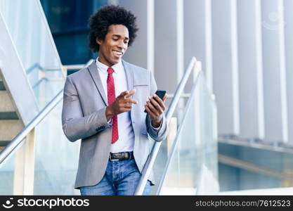 Black Businessman using his smartphone near an office building. Man with afro hair.. Black Businessman using a smartphone near an office building