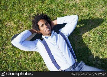 Black businessman with afro hair resting lying on the grass with his skateboard. Black businessman resting lying on the grass with his skateboard