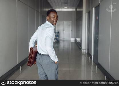 Black businessman with briefcase in office hall. Successful business person walking down the corridor, black man in formal wear. Black businessman with briefcase in office hall