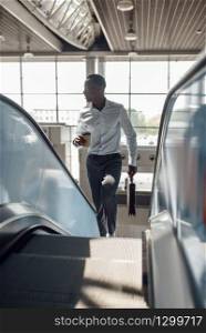 Black businessman with briefcase talking by phone on the escalator in mall. Successful business person, black man in formal wear, shopping center. Businessman talking by phone on escalator in mall