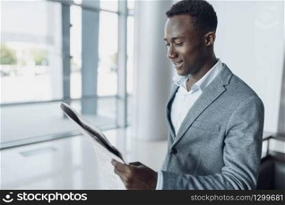 Black businessman with newspaper in office building. Successful business person, black man in formal wear. Black businessman with newspaper, office building