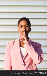 Black businesswoman doing silence gesture. African american female wearing suit with pink jacket with sunset light.. African American business woman doing silence gesture.