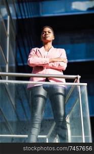 Black businesswoman standing near business office building. African american female wearing suit with pink jacket.. African businesswoman standing near business office building.