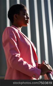 Black businesswoman standing near business office building. African american female wearing suit with pink jacket.. Black businesswoman standing near business office building.