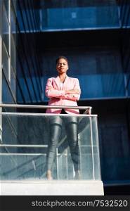 Black businesswoman standing near business office building. African american female wearing suit with pink jacket.. African businesswoman standing near business office building.