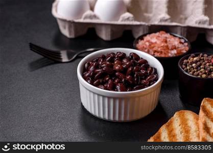 Black, canned beans in a white saucer against a dark concrete background. Ingrient for vegitarian cooking. Black, canned beans in a white saucer against a dark concrete background