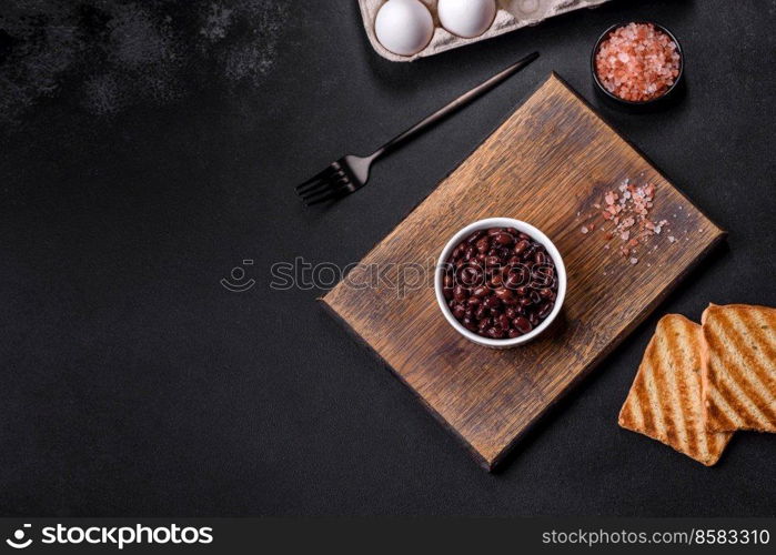 Black, canned beans in a white saucer against a dark concrete background. Ingrient for vegitarian cooking. Black, canned beans in a white saucer against a dark concrete background