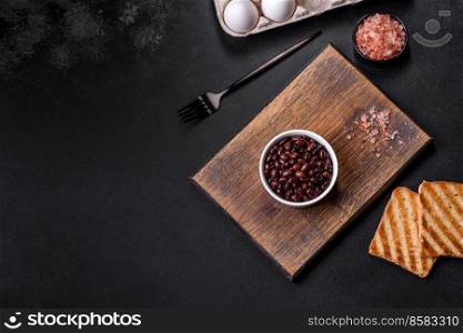 Black, canned beans in a white saucer against a dark concrete background. Ingrient for vegitarian cooking. Black, canned beans in a white saucer against a dark concrete background